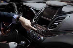 A representative from General Motors opens a compartment inside a Chevy Impala while demonstrating the MyLink connection and entertainment system.