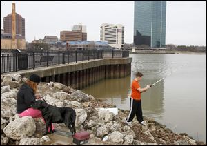 Nancy Thomas of Toledo, with her dog Jade, joins her son Tyler Thomas, 12, as he puts his Christmas-gift fishing rod to the test at International Park across from downtown.