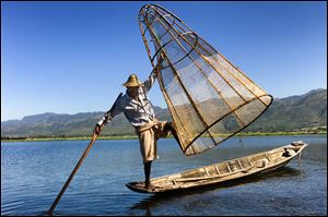 A fisherman does a balancing act with his boat, net, and oar in Inle Lake, Myanmar.