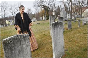 Sylvania Area Historical Society board member Mimi Malcolm inspects the inscription on a tombstone as she walks through the area. Ms. Malcolm said graves in the cemetery date to the early 1800s, but there are several unmarked graves that date back even further. 