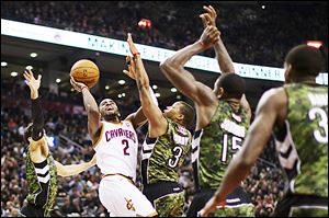 The Cavaliers' Kyrie Irving (2) shoots against the Raptors' Landry Fields, left, Kyle Lowry (3), and Amir Johnson (15) during the first half.