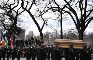 A casket containing the body of former New York City Mayor Ed Koch is loaded into a hearse while city employees, politicians, media watch after his funeral in New York.