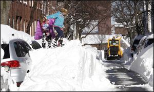 Riley Clark, left, and her sister Mckenzie play on top of a pile of snow as a snow removal machine clears a path in Boston. The city recorded 24.9 inches of snow, its fifth-largest snowstorm on record. 