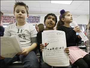 Second-graders Anthony Kovacs, 8, left, Nikhil Methi, 6, and Adrianna Magers, 8, hold papers with ideas about ways they could help people in their communities as they listen to a presentation at Woodland Elementary.by Robin Laird, Hannah’s Socks board member and assistant principal at the junior high.