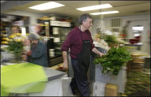 Mary Ann Myers, of Sylvania, left, puts the finishing touches on an order while Ken Myrice carries greens for floral arrangements at Emery's Flowers & Company.