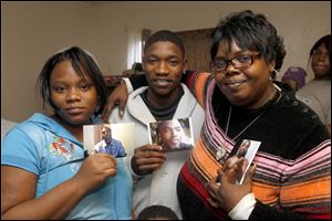 Some of La’Sean Robinson’s siblings show pictures of the murder victim. From left are Latosha, James, and Lautricia Robinson, gathered in Toledo.
