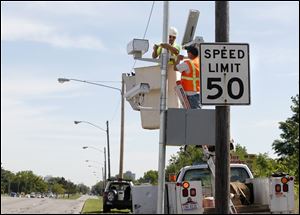 Andy Orshoski of National Light and Power in Sandusky, left, and David Burnham of Redflex Traffic Systems, Phoenix, install a speed monitoring camera on the Anthony Wayne Trail in Toledo.