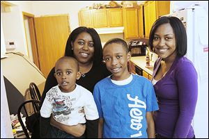 Danielle Peace, left, holds her son Sean, 4, as she and her son Kenny, 12, and daughter Kai, 18, right, pose for a photograph in their kitchen. Peace has lived in her home on Fulton Street in Toledo since 1998. She is hoping to purchase the home, where she lives with her four children, through the Low Income Housing Tax Credit program.