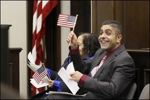 Ahmed Bdair, of South Toledo, right, waves his American flag after receiving his paperwork and taking the oath of citizenship early today during a naturalization ceremony at the Federal Courthouse in downtown Toledo.