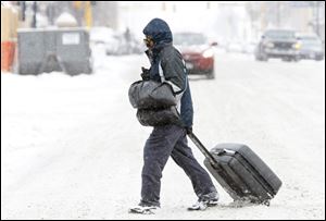 Maury Lawson drags his suitcase through the snow Monday while crossing N.P. Avenue in Fargo, N.D., on his way to the bus depot.