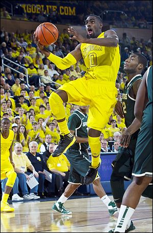 Michigan’s Tim Hardaway, Jr., leaps past Michigan State’s Branden Dawson, right, for a basket. UM has unlikely fans as OSU will root for them to beat Indiana.