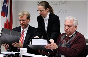 Meghan Gallagher, director of the Lucas County Board of Elections, hands binders to board member Jon Stainbrook, left, and board chairman Ron Rothenbuhler during the board's meeting.