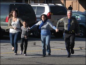 In this Dec. 14, 2012 file photo provided by the Newtown Bee, a police officer leads two women and a child from Sandy Hook Elementary School in Newtown, Conn., shortly after Adam Lanza opened fire, killing 26 people, including 20 children.