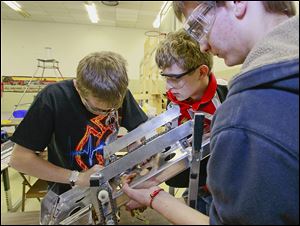 Mark Damazyn, left, Charlie Cook, center, and Matt Stewart of the Bedford Express team work on the shooter for the Frisbee-throwing part of the competition, one of two functions the robot is to perform.