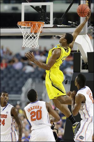 Michigan's Glenn Robinson III dunks as Florida's Michael Frazier II (20), Casey Prather (24) ,and Will Yeguete (15) look on during the second half of a regional final game in the NCAA college basketball tournament in Arlington, Texas.