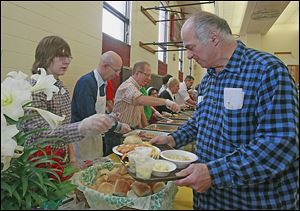 Chase Smith, 15, of Macomb, Mich., left, serves William Stowe of Toledo a roll as part of the dinner.   Christ the King Church hosts a free Easter Sunday dinner for all who want to attend.