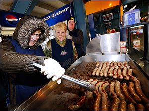 Carol Vargo turns bratwursts as Cody Witt, right, tries to warm the ears of his grandmother Alice Witt during opening day for the Toledo Mud Hens at Fifth Third Field. 