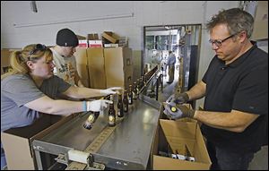 Shannon Mohr, brewery manager, Chad Bukowski, bottler, and Matt Snyder, Middle Grounds market manager, pack bottled beer as it comes off the production line at the Maumee Bay Brewing Co.