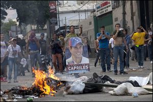 Demonstrators, one holding a poster of opposition presidential candidate Henrique Capriles, confront riot police from behind a burning barricade in the Altamira neighborhood in Caracas, Venezuela, Monday.
