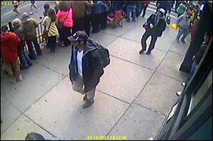 A surveillance image released by the FBI of the Boston Marathon bombing suspects, a man in a black baseball cap and the man behind him on the sidewalk in a white cap.