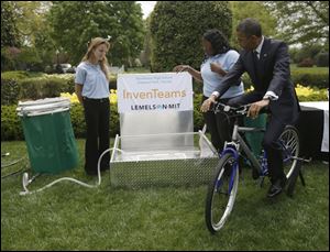 President Barack Obama pedals bicycle-powered emergency water-sanitation station for Payton Karr, 16, left, and Kiona Elliott, 18, center, to help demonstrate their invention.