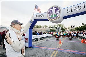 Tom Falvey holds a U.S. flag as the national anthem is played before the start of the 2012 Glass City Marathon.
