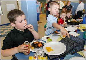 Patrick Ford eats a chicken nugget while Alejandro Lucio points to an item he liked on another first grader's plate. 