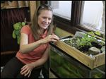  Laura Schetter next to a fish tank with tilapia. On top is a garden. The water from the tank goes into the garden, where the roots of the plants clean the water which is then returned to the tank.
