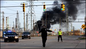 A  Melvindale police officer in a haz-mat mask directs traffic as a fire burns at the Marathon refinery in Detroit after an explosion April 27. 