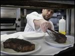  Chef Tim Childers places a 10-ounce filet mignon onto a plate a plate next to a 14-ounce New York strip at Rockwell's.