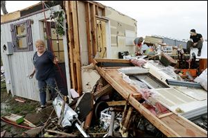 Marlena Hodson walks out of her home as her grandsons, Campbell Miller, 10, and Dillon Miller, 13, at right, help her sort through belongings after a tornado damaged her home Carney Okla., on Sunday.