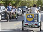  Maxwell Austin, owner of Glass City Pedicabs, gives passenger Matt Rowland a ride while he passes employee Brittany Ryan, right, on the street.