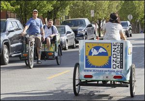 Maxwell Austin, owner of Glass City Pedicabs, gives passenger Matt Rowland a ride while he passes employee Brittany Ryan, right, on the street.