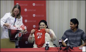Dr. Tracy Manuck, left, gives a baby present to Guillermina and Fernando Garcia today after  a news conference at the University of Utah hospital, in Salt Lake City.