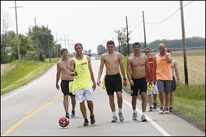 Derek Garde, left, Nick Streibick, center left, Isaac Beal, center, and Jake Essig, center, right, walk along U.S. 127 near Fulton County’s Fayette on the 11th day of their walk, Thursday. The four are kicking a soccer ball along a 250-mile route. They call themselves Dribble 4 Toledo.  