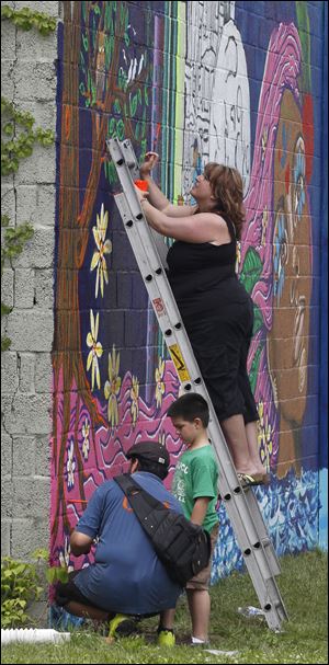 Jennifer Jacobs, the CEO of the Providence Center, helps paint the mural on the exterior walls of the center on Broadway Street.