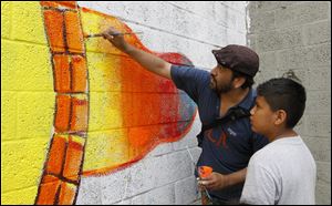 Ricardo Quinonez Aleman and Juan Ferime, 10, of Adrian, work on the mural at the Providence Center. The Organization of Latino Artists sponsored the project. 