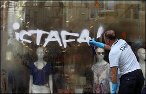 A man cleans graffiti reading 'Resign from a storefront on Istiklal Street, Istanbul's main shopping strip today.