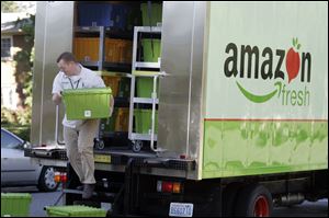 An Amazon Fresh worker delivers groceries in Seattle, where the ecommerce giant has deployed a fleet of 12 trucks to test its new service.  Customers also can pick up grocery orders at certain sites.