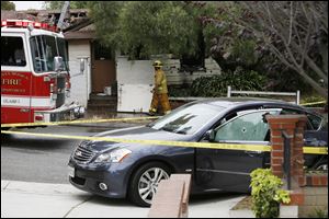 A firefighter walks past a car with bullet holes across a home that caught fire in Santa Monica, Two people were found dead at the house. 