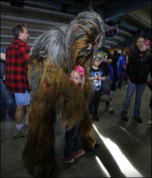 Abby Kurdziel, 4, gets a hug from Chewbacca on the concourse before a Toledo Mud Hens game May 4. Transportation Security Administration agents in Denver briefly stopped “Star Wars” franchise actor Peter Mayhew, who plays Chewbacca, recently as he was boarding a flight with a cane shaped like one of science-fiction’s most iconic weapons.