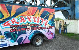 Andrew Kirk, left, and Takisha Townsend, of Toledo’s Neighborhood Beautification Action program, remove graffiti in International Park as the Operation Wipeout Graffiti Removal Unit is unveiled.