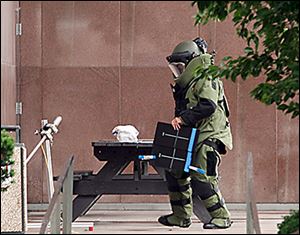 A Toledo police bomb squad member inspects a suspicious package on a table outside One Government Center.