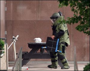 A member of the Toledo Police Bomb Squad investigates a suspicious package left on a picnic table outside One Government Center.