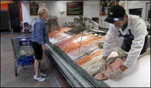 Mary Pat Perlinski, of Lambertville, shops at the Seafood Market as employer Joe Salazar stocks freshly-sliced  salmon at the Kroger store in Lambertville, Mich.