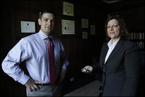 The University of Toledo's military liaison Lt. Haraz Ghanbari, left, stands with Patty James, director of senior administrative operations, right, as she holds the prisoner of war bracelet she received as a Christmas gift at the age of 14. 