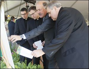 Kurt Darrow, chairman, president, and CEO of La-Z-Boy Inc., second from right, points out features of the site plan for the company’s new headquarters to, from left, the Rev. Bryan Meldrum of Monroe, the Rev. Jim Smalarz, pastor of St. John Catholic Church, and the Rev. Terrence Kerner, pastor of St. Joseph and St. Martha churches. The building is on land acquired from the Sisters, Servants of the Immaculate Heart of Mary, a Catholic religious order that was founded in Monroe in 1845.