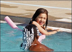 Jessica Bateman, 8, holds onto the side as she and friend Saniya Lincoln-Adams, 9, cool off Monday at Pickford Pool. Six of the city of Toledo’s public pools opened Monday.