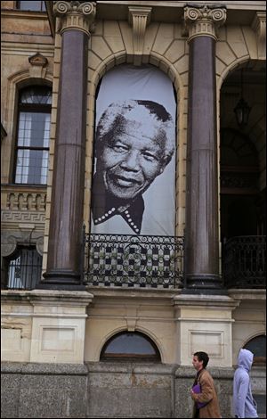 Pedestrian's walks beneath a giant portrait outside the City Hall in Cape Town, South Africa, Monday, June 24, 2013 at the spot where, on the balcony, former South Africa president Nelson Mandela, made his first public speech after being released from 27-years imprisonment.