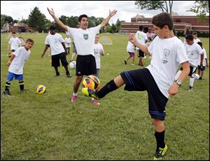 Yadi Aliakbar of the Toledo Celtics Soccer Club, left, cheers as Yasir Jallad, 10, completes a challenge during a mini soccer camp.